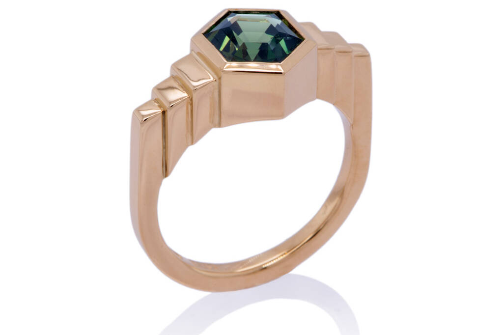 Ziggurat ring set with a blue-green parti-sapphire standing upright against a white background.